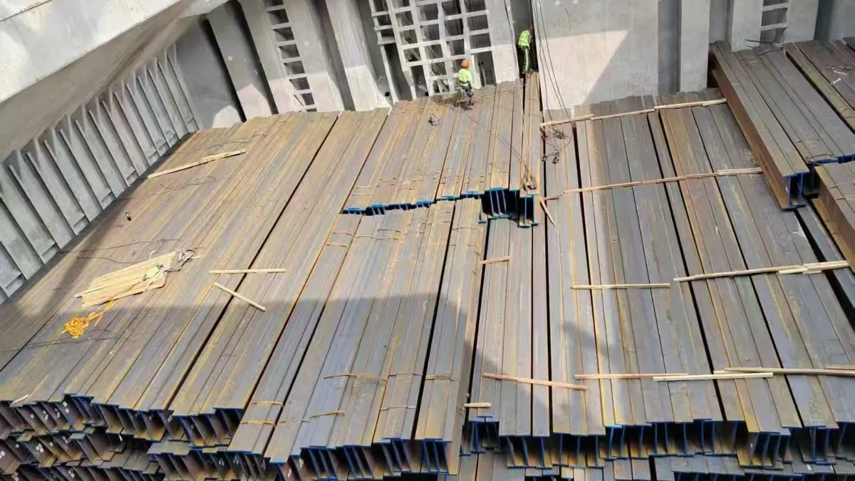 Structural H-beams with blue-painted ends being stowed in a cargo hold with wooden dunnage